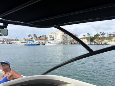 A woman relaxes on the deck of a boat at a marina, enjoying the waterfront views and the vibrant surroundings.