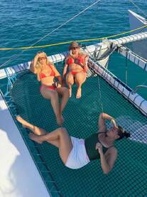 Three friends relax on the netting of a catamaran, enjoying the sun and sea — a perfect moment for fun and relaxation on the water.