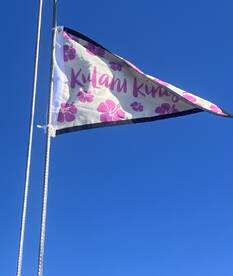 A flag with the name 'Kulani Kinis' against a clear blue sky, showcasing a nautical theme.