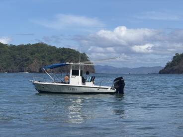 A small boat named 'La Pola' is anchored in calm waters, with two individuals onboard enjoying a day of fishing and adventure in a scenic coastal setting.