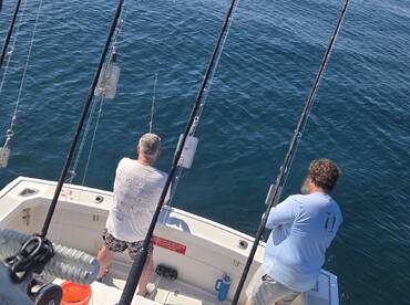 Two anglers enjoy a day of fishing on the open ocean, showcasing the thrill of deep-sea adventures aboard a fishing boat.