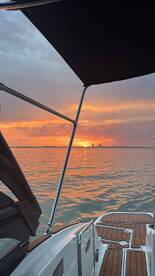 A serene sunset view from the deck of a boat, showcasing the tranquil waters and skyline in the distance — perfect for evening cruises.