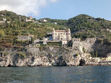 A stunning view of a historic castle perched on a cliffside, surrounded by lush greenery along the coastline — a picturesque destination for boat tours.