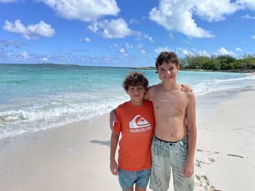 Two boys enjoy a sunny day at the beach, capturing a moment of friendship against the beautiful ocean backdrop — perfect for family vacation memories.
