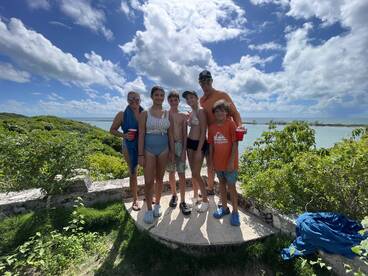 A cheerful family poses together against a stunning backdrop of lush greenery and blue waters, capturing a memorable moment during their boating adventure.