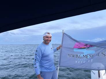 A man proudly holds a flag for 'Making Memories Charters' in the beautiful waters of Key West, showcasing the spirit of adventure on the ocean.