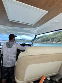 A view of the helm inside a boat, showcasing the seating and dashboard as a person navigates through scenic waters.
