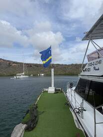 A serene view of a docked boat with a vibrant flag, set against a backdrop of lush hills and cloudy skies, perfect for showcasing the beauty of marine life.