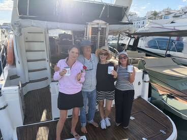 A cheerful group enjoys drinks on the deck of a yacht, celebrating together in a picturesque marina setting.