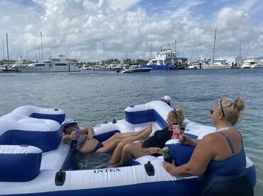 A group of friends relaxes on a floating mat at a marina, enjoying drinks and the sun — the perfect setting for a fun day on the water.