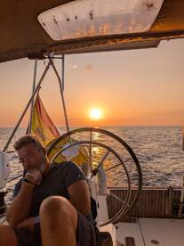 A sailor relaxes at the helm of a yacht during a stunning sunset, capturing the essence of peaceful sailing adventures on the open water.