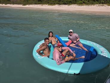 A lively group enjoys a day on a floating mat in crystal-clear waters, perfect for relaxation and fun under the sun.