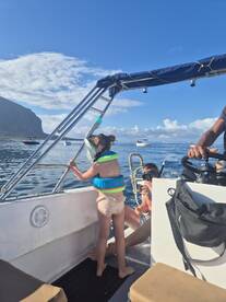 A young girl in a life jacket leans over the side of a boat, excitedly observing the ocean, while an adult prepares for snorkeling — a perfect family adventure on the water.