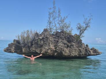A man enjoys a refreshing swim near a rocky outcrop in clear turquoise waters, showcasing the beauty of tropical destinations.