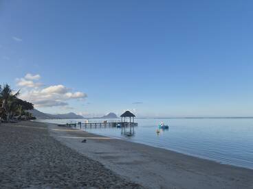 A serene beach scene featuring a wooden pier extending into calm waters, framed by lush greenery and distant mountains — an ideal destination for relaxation and scenic views.