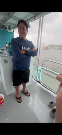 A man stands on the deck of a boat during a rainy day, showcasing the relaxed atmosphere of a boating experience, even in less-than-ideal weather.