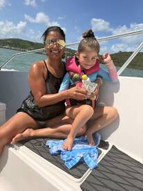A joyful moment on the water as a mother and daughter enjoy their time aboard a boat, both wearing life jackets and sharing a snack — perfect for family adventures.