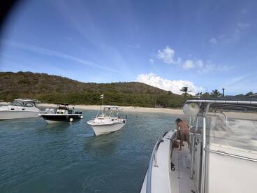 A lively scene at the beach with multiple boats anchored, showcasing guests enjoying the water and sun — perfect for a fun day out on the water.